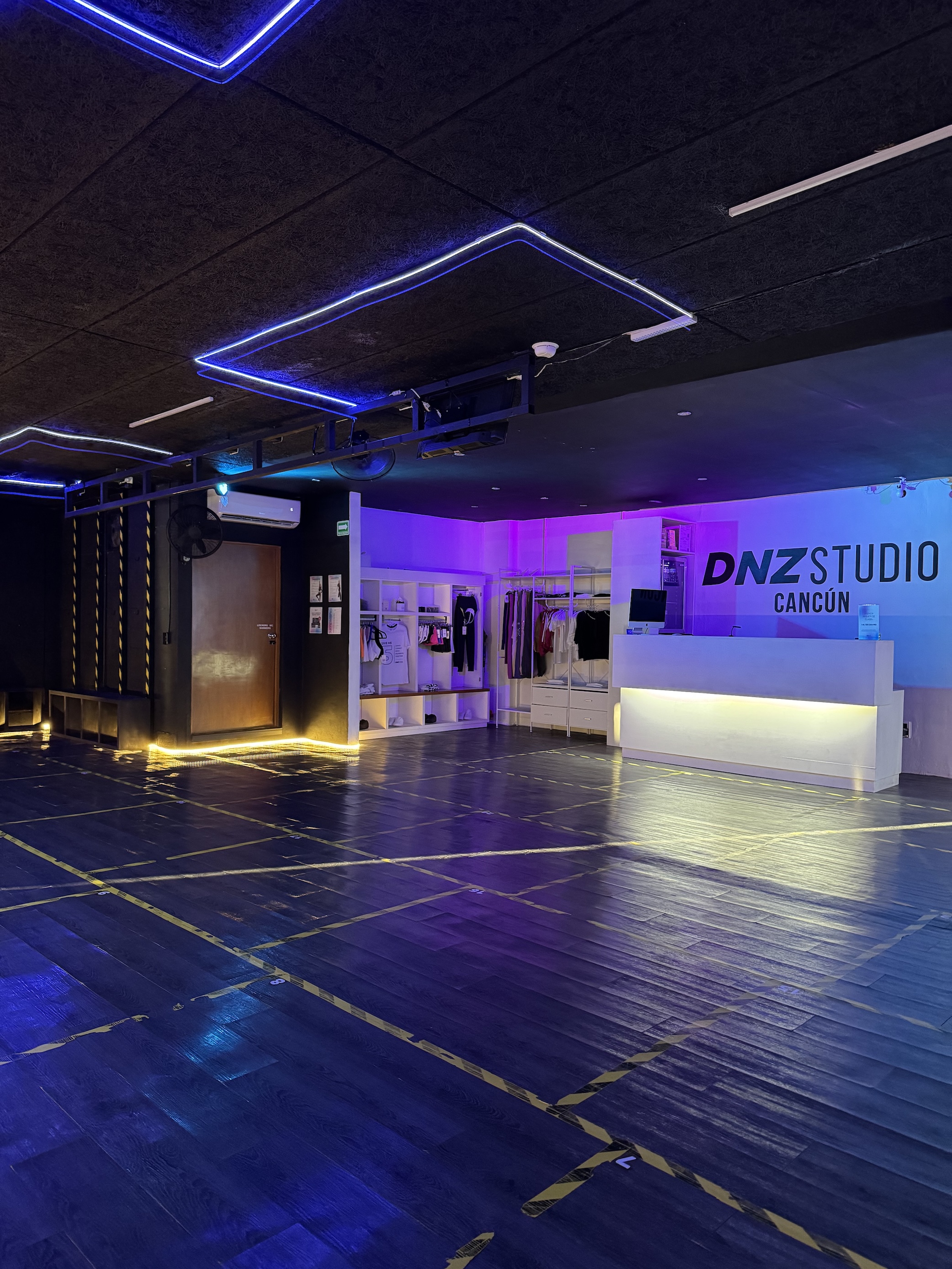 Interior de DNZ Studio Cancún: duela, neón y la recepción con el letrero de la sede
